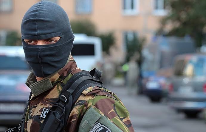An unidentified security professional in a balaclava and field uniform, photographed on a street